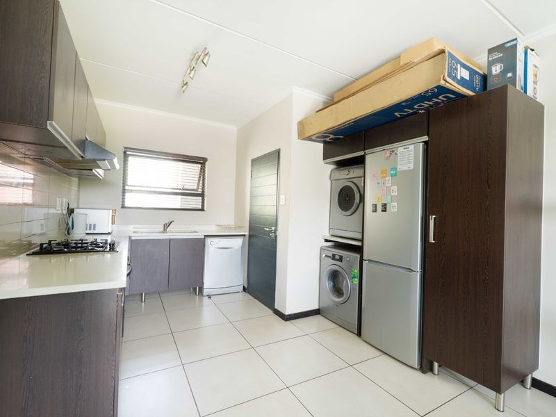 A functional kitchen featuring dark wood cabinetry, a gas hob, extractor fan, and integrated laundry space with tiled flooring throughout.