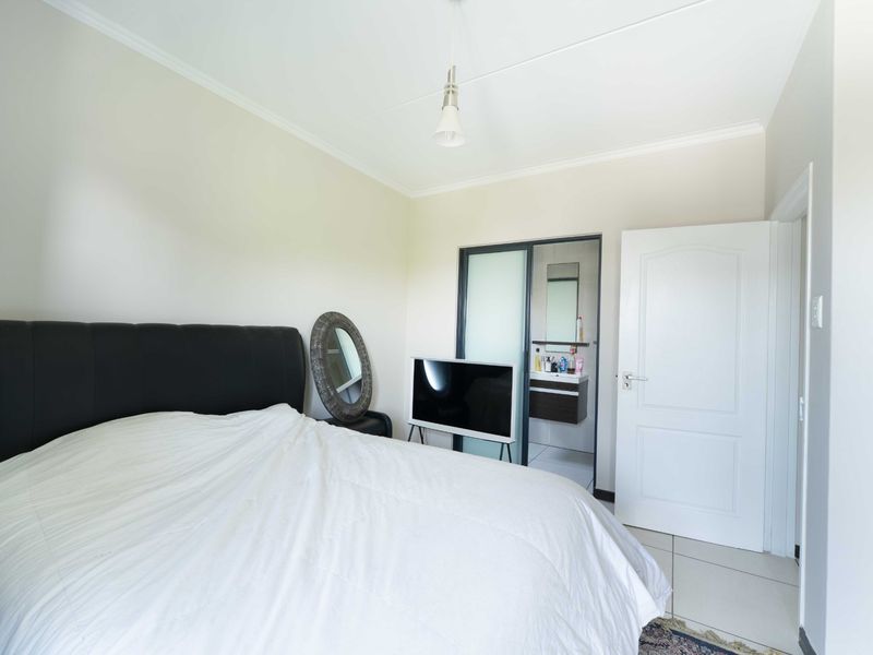 A well-maintained bedroom featuring tiled flooring, coved ceilings, and direct access to an en-suite bathroom through a sliding glass door.