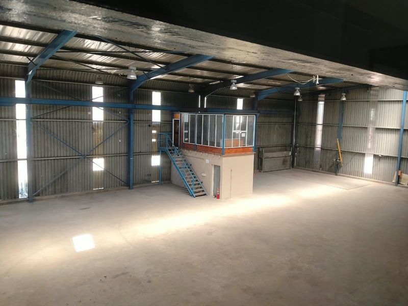 Spacious industrial warehouse featuring a steel portal frame, concrete flooring, and an elevated mezzanine office pod with integrated staircase access.