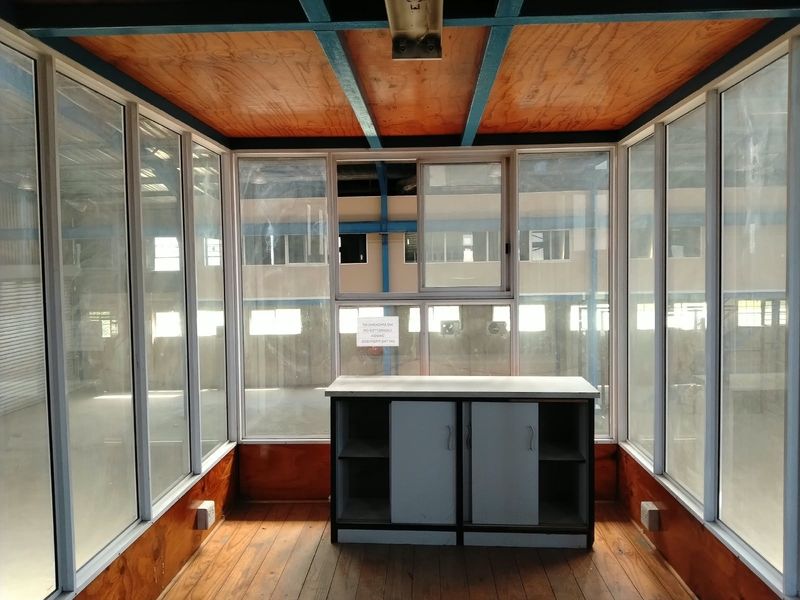 A small, enclosed office or security booth featuring timber paneling, large glass windows, and built-in storage cabinetry.