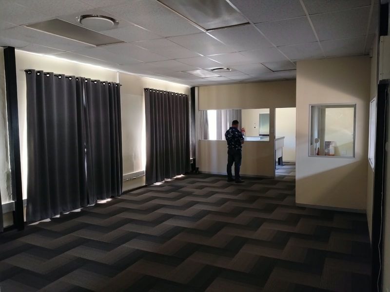 Spacious office area featuring a suspended ceiling, recessed lighting, and patterned carpet flooring with an internal glass partition and service window.