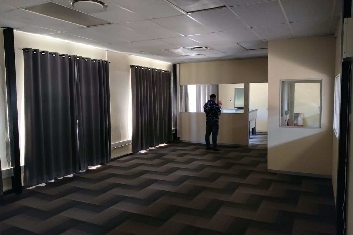 Spacious office area featuring a suspended ceiling, recessed lighting, and patterned carpet flooring with an internal glass partition and service window.