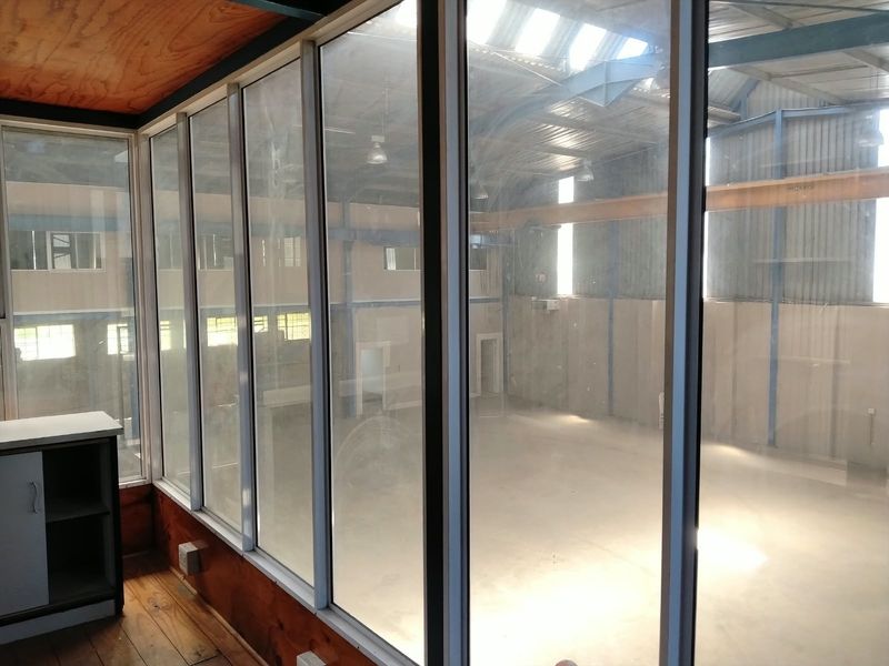 An interior view from an office space looking out over a large, open-plan industrial warehouse area with high ceilings and steel structural elements.