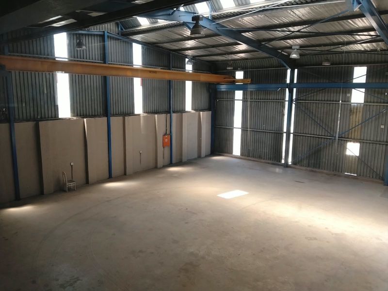 Spacious industrial warehouse featuring high ceilings, concrete flooring, corrugated metal walls, and an integrated overhead gantry crane, suitable for various commercial or storage operations.