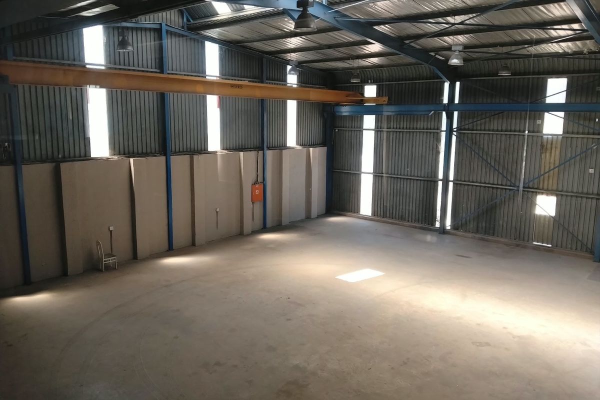 Spacious industrial warehouse featuring high ceilings, concrete flooring, corrugated metal walls, and an integrated overhead gantry crane, suitable for various commercial or storage operations.