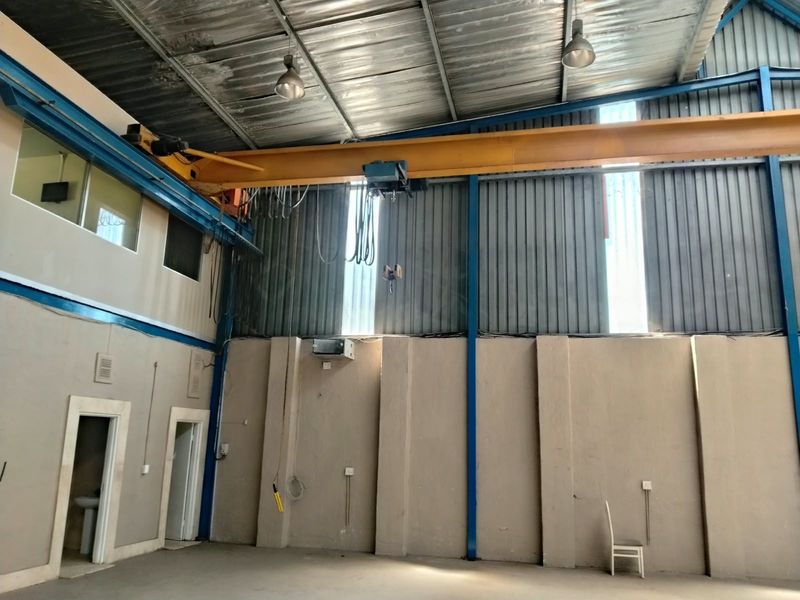 Spacious industrial warehouse area featuring high ceilings, an integrated overhead gantry crane, and durable concrete flooring, suitable for various commercial or manufacturing operations.