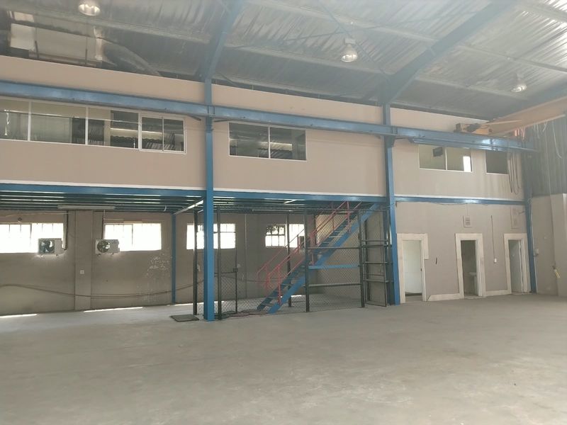 Spacious industrial warehouse featuring a mezzanine level, steel staircase, exposed structural beams, and concrete flooring, suitable for various commercial or storage applications.