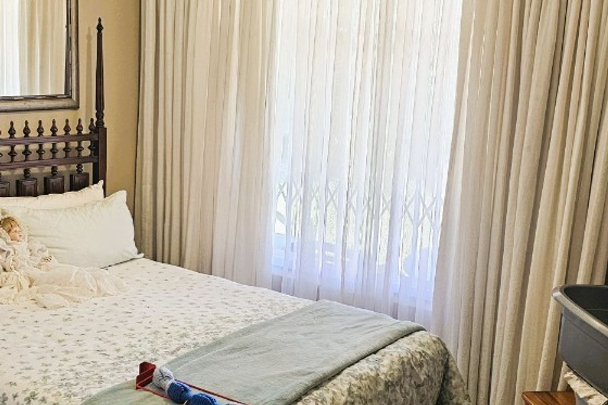 A bedroom featuring tiled flooring, a ceiling fan, and floor-to-ceiling curtains covering a window with a security gate.