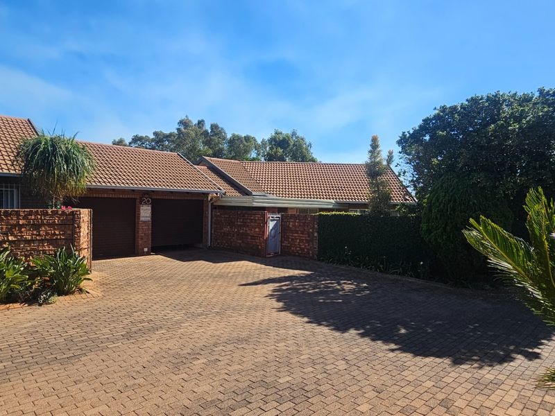 Front exterior view of a townhouse featuring a double garage, brick paved driveway, and established garden surroundings.