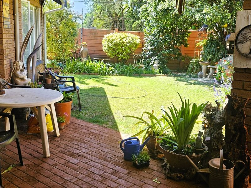 A covered brick-paved patio area overlooking a private garden with established landscaping and perimeter fencing.