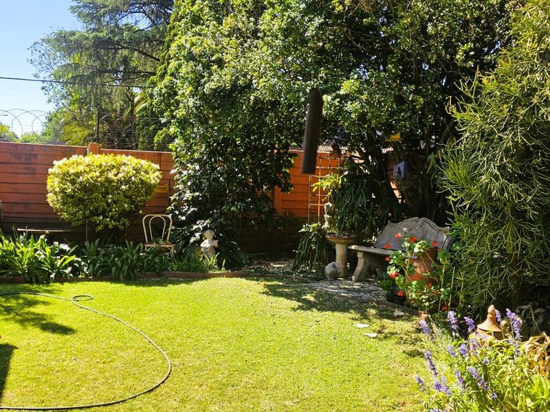 A well-maintained private garden featuring a lush green lawn, mature trees, and established perimeter fencing.