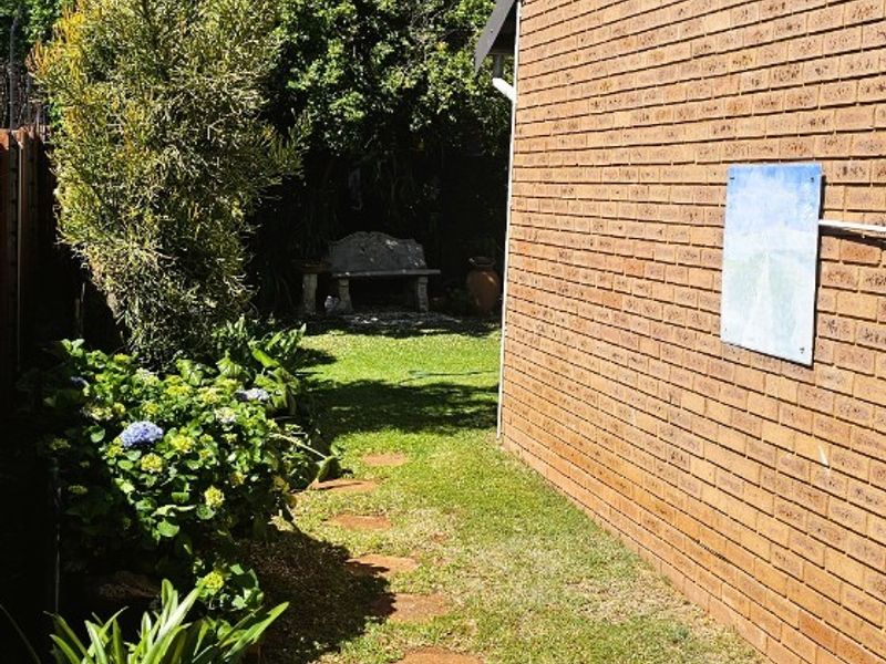 A side garden pathway featuring a brick wall facade, stepping stones, and established greenery leading to a rear outdoor area.