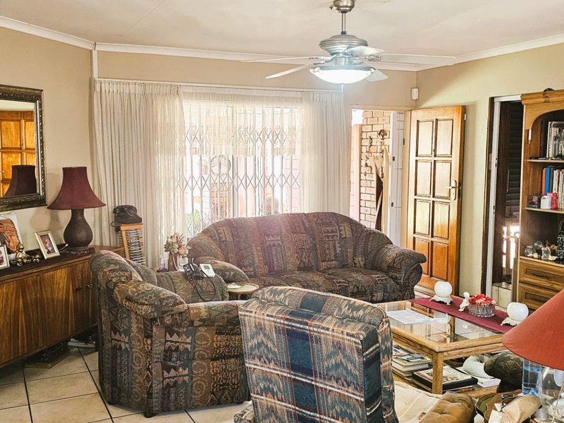 A comfortable living room featuring tiled flooring, a ceiling fan, and a sliding door with a security gate leading to the exterior.