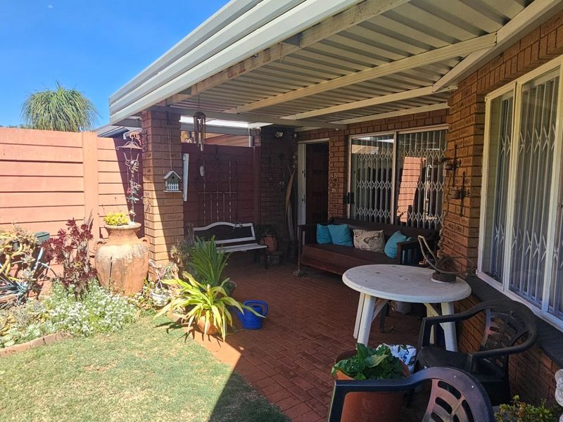 A covered brick-paved patio area featuring brick pillars and security gates, providing a functional outdoor space adjacent to the garden.