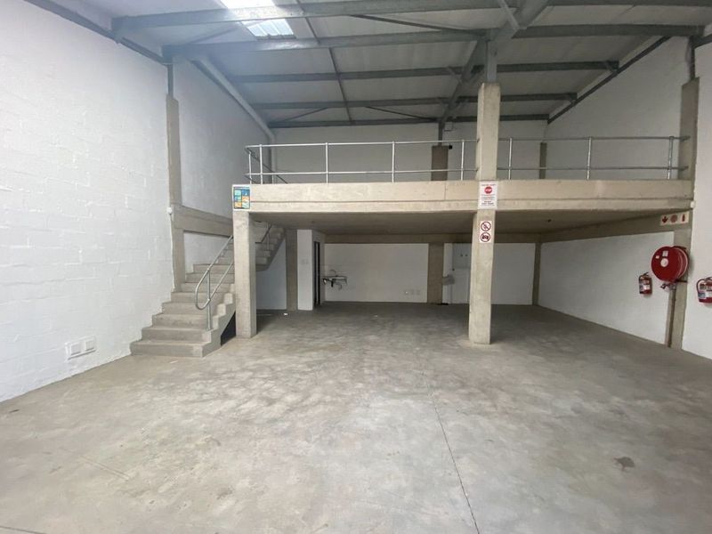 Spacious industrial warehouse unit featuring a concrete mezzanine level, staircase, exposed steel roof structure, and basic utility sink, suitable for storage or workshop use.
