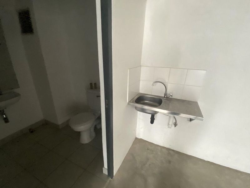 A functional industrial-style bathroom area featuring a wall-mounted stainless steel sink, a standard ceramic toilet, and a separate pedestal basin.