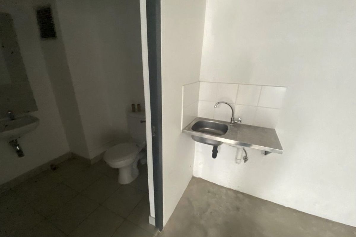 A functional industrial-style bathroom area featuring a wall-mounted stainless steel sink, a standard ceramic toilet, and a separate pedestal basin.
