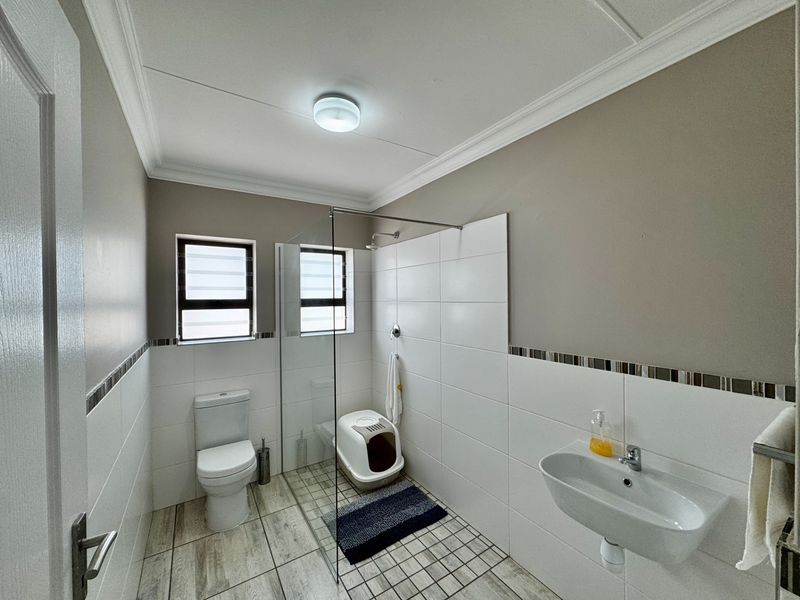 A modern, well-maintained bathroom featuring a glass shower enclosure, wall-mounted basin, and neutral tiled finishes throughout.