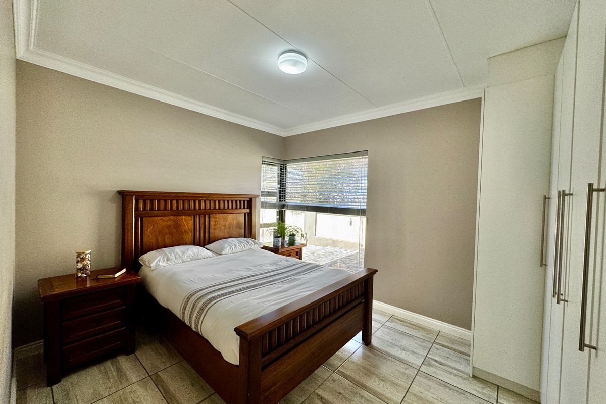 A well-maintained bedroom featuring neutral wall tones, tiled flooring, built-in cupboards, and venetian blinds, offering a clean and functional living space.