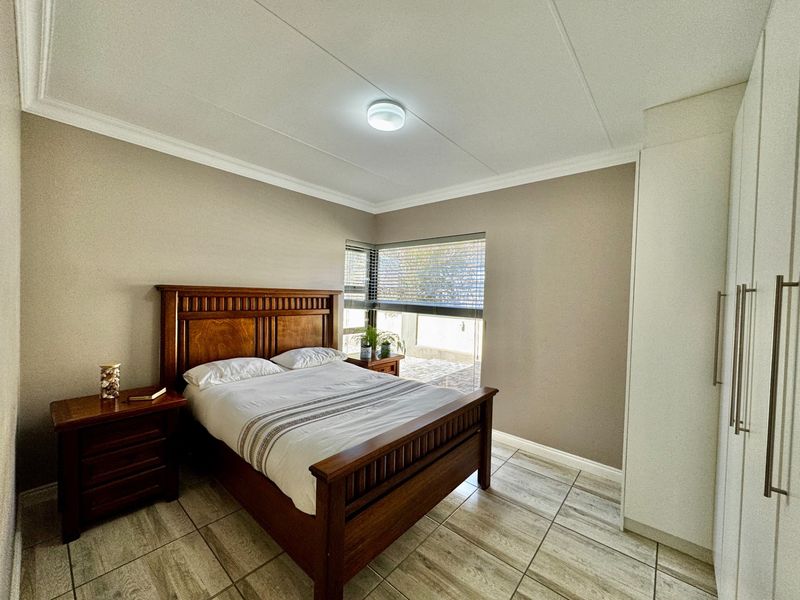 A well-maintained bedroom featuring neutral wall tones, tiled flooring, built-in cupboards, and venetian blinds, offering a clean and functional living space.
