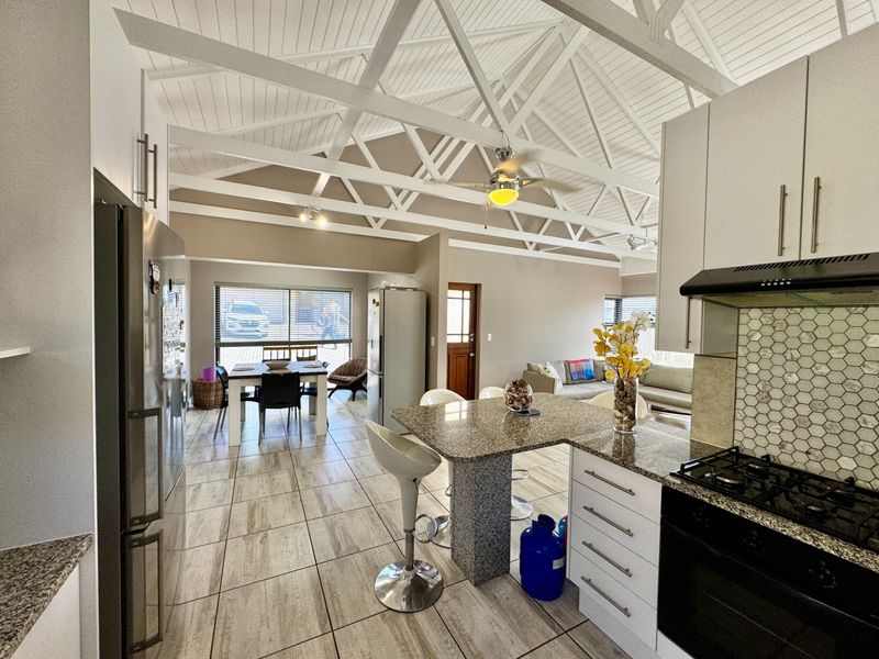 Spacious open-plan living and kitchen area featuring high vaulted ceilings with exposed trusses, granite countertops, and modern tiled flooring throughout.