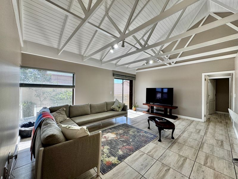 Spacious living room featuring high exposed timber truss ceilings, neutral wall tones, and large windows providing ample natural light with direct access to the exterior.