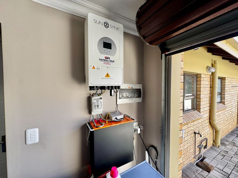 Garage interior featuring a wall-mounted Sunsynk solar inverter and battery storage system, with a roller shutter door and brick exterior wall visible.