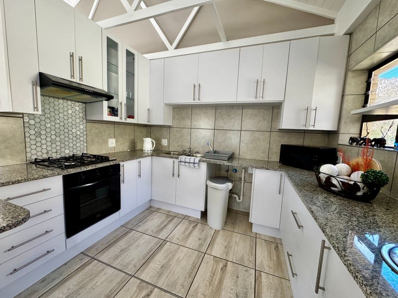 Modern kitchen featuring white cabinetry, granite countertops, gas hob, built-in oven, and distinctive exposed roof trusses, providing a bright and functional workspace.