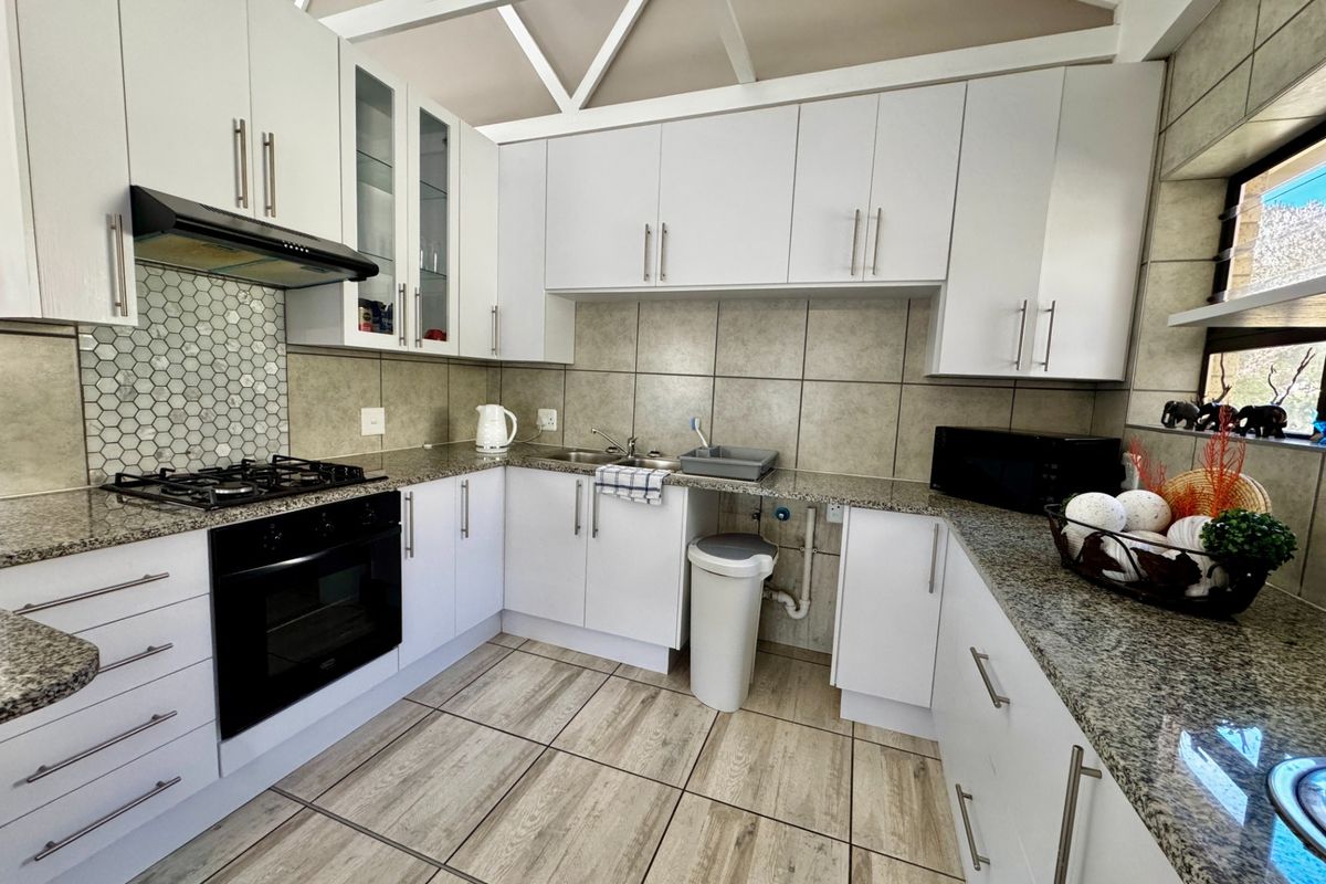 Modern kitchen featuring white cabinetry, granite countertops, gas hob, built-in oven, and distinctive exposed roof trusses, providing a bright and functional workspace.