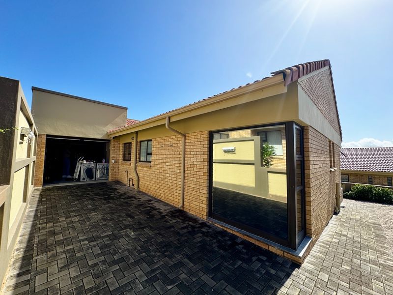 Rear exterior view of the townhouse featuring a brick facade, paved driveway, and an integrated garage with tiled roofing.
