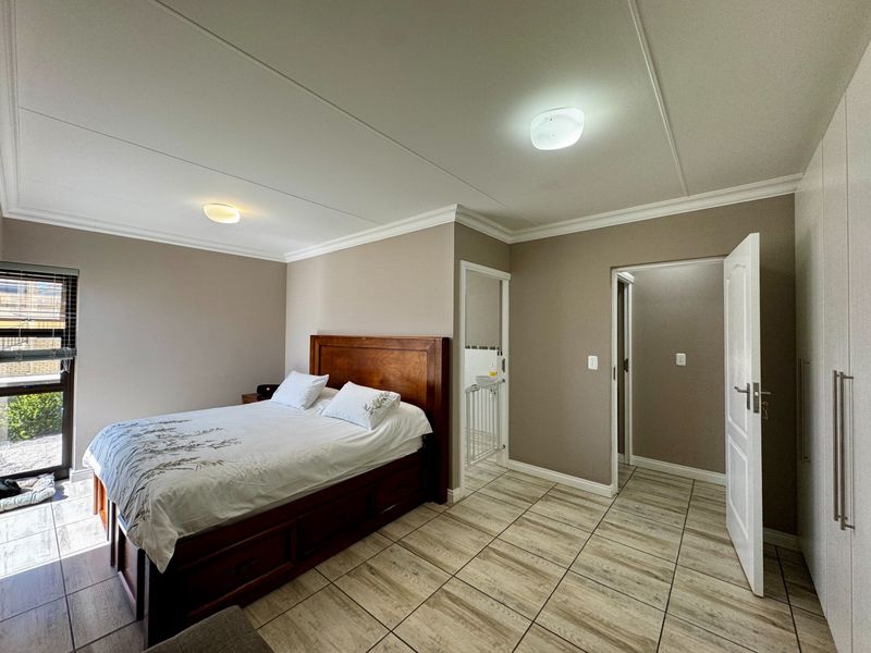 A well-maintained bedroom featuring tiled flooring, built-in cupboards, and neutral wall tones, with direct access to an en-suite bathroom.