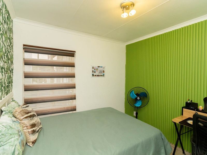 A bedroom featuring a textured green accent wall, patterned wallpaper, and roller blinds, providing a functional space with neutral flooring.