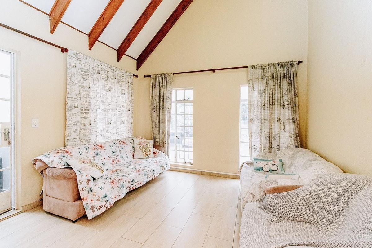 A bright living room featuring a high vaulted ceiling with exposed timber beams, tiled flooring, and large windows providing ample natural light.