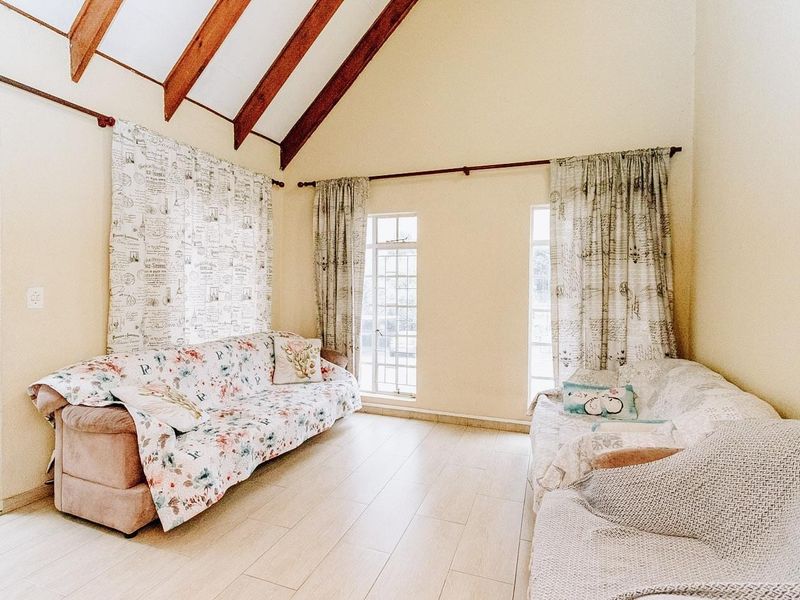 A bright living room featuring a high vaulted ceiling with exposed timber beams, tiled flooring, and large windows providing ample natural light.