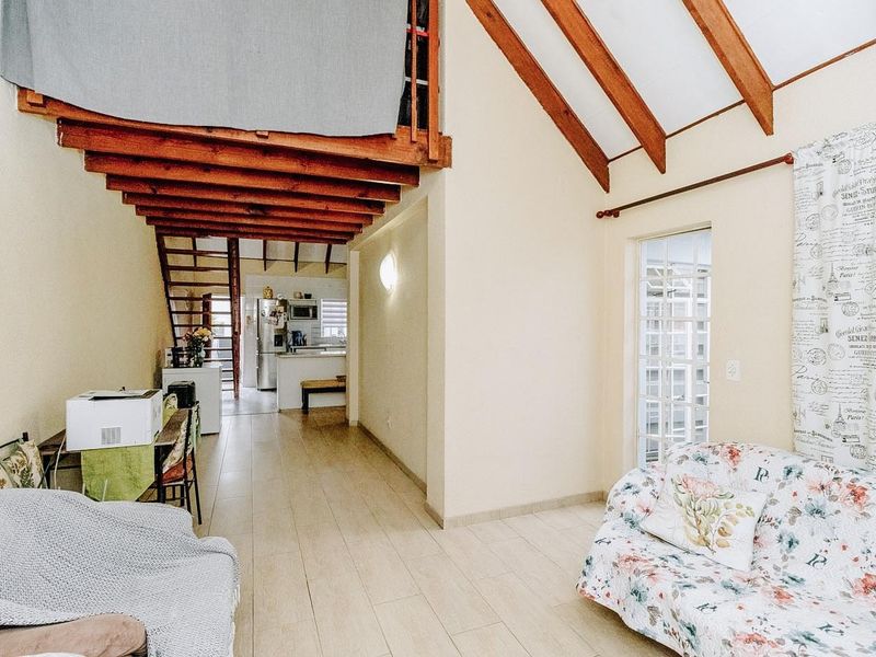 Open plan living area featuring high vaulted ceilings with exposed timber beams, tiled flooring, and a mezzanine level overlooking the kitchen space.