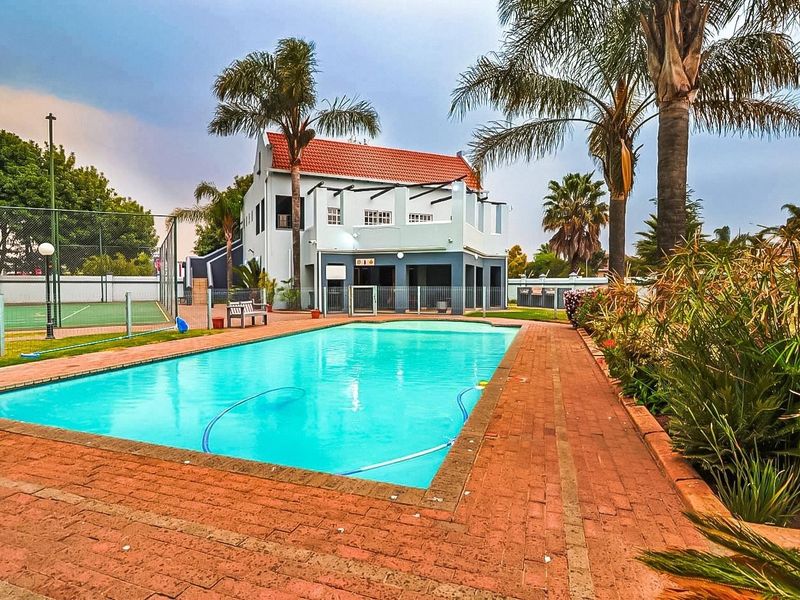 A well-maintained communal pool area featuring brick paving, adjacent tennis court, and established landscaping within a townhouse complex.