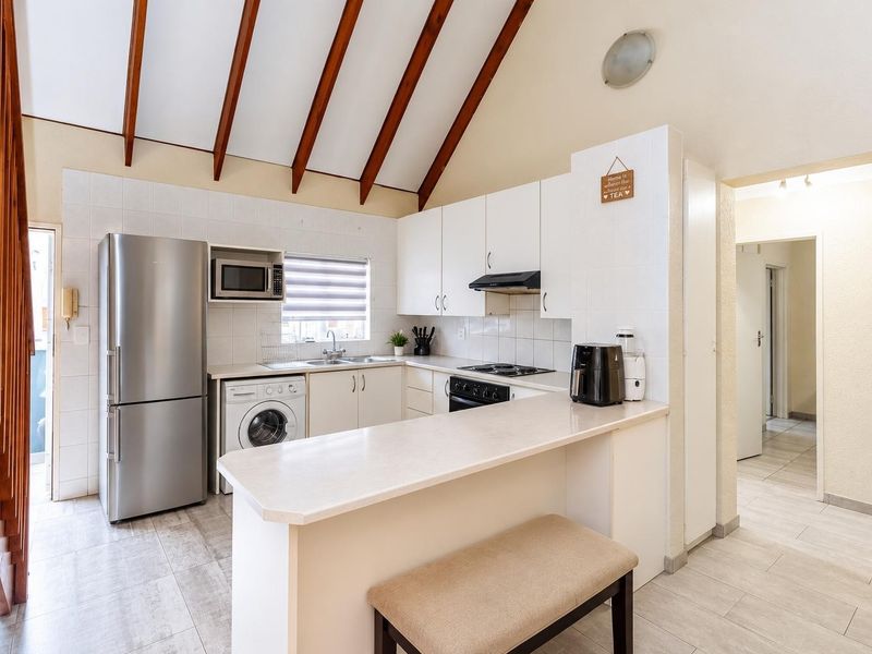 A functional kitchen featuring white cabinetry, laminate countertops, a breakfast bar, and exposed timber ceiling beams, complemented by tiled flooring.