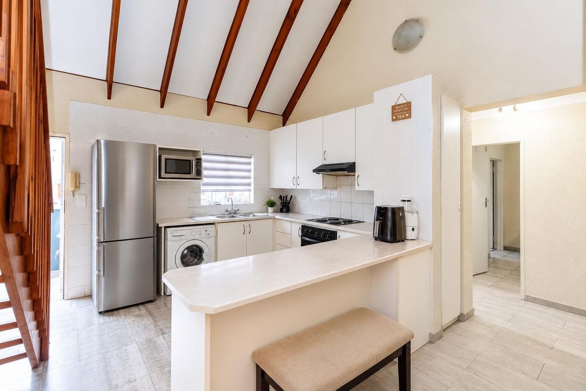 A functional kitchen featuring white cabinetry, laminate countertops, a breakfast bar, and exposed timber ceiling beams, complemented by tiled flooring.
