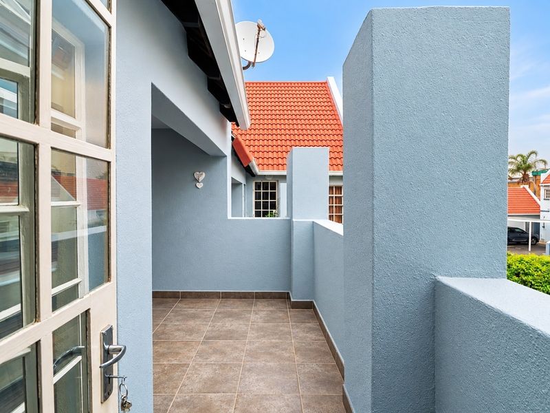 A clean, well-maintained balcony featuring tiled flooring and a solid parapet wall, accessible via a classic french door.