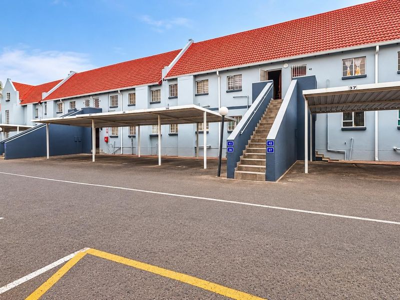 Front exterior view of a townhouse complex featuring covered parking bays, external staircases, and a tiled roof.