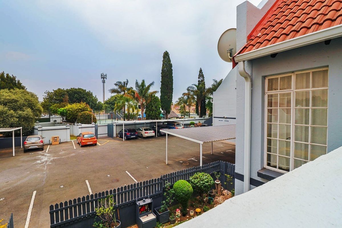 View of the townhouse exterior featuring a paved parking area with carports, perimeter fencing, and a tiled roof structure.