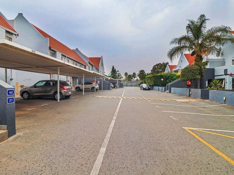 View of the townhouse complex driveway featuring covered parking bays and well-maintained exterior building facades with tiled roofing.