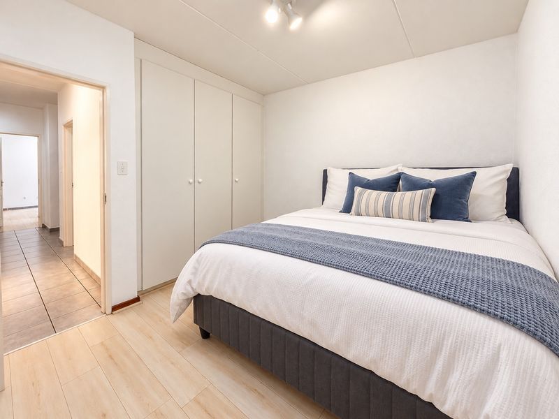 A well-maintained bedroom featuring light laminate flooring, built-in cupboards, and neutral finishes, providing a clean and functional living space.