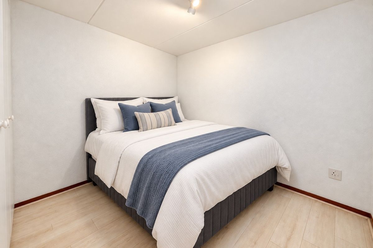 A clean and well-maintained bedroom featuring light-toned laminate flooring, a built-in cupboard, and modern ceiling spotlighting.