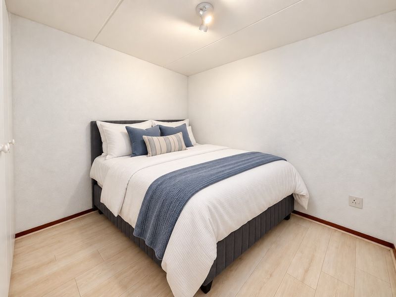 A clean and well-maintained bedroom featuring light-toned laminate flooring, a built-in cupboard, and modern ceiling spotlighting.