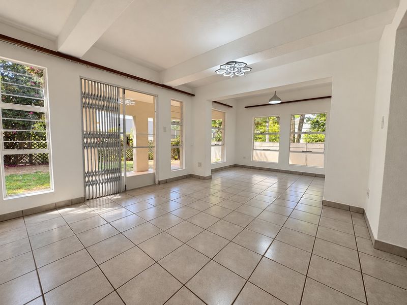 A bright and spacious open-plan living area featuring neutral tiled flooring, large windows for natural light, and secure access to the outdoor space.