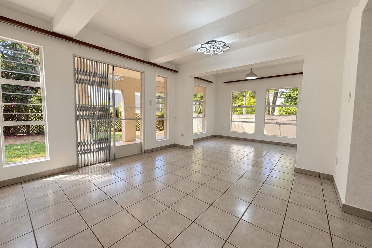 A bright and spacious open-plan living area featuring neutral tiled flooring, large windows for natural light, and secure access to the outdoor space.