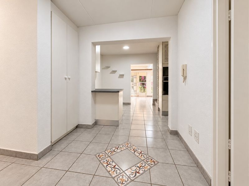 A bright, tiled hallway featuring built-in storage cupboards, a breakfast counter, and an intercom system, leading through to an open-plan living area.