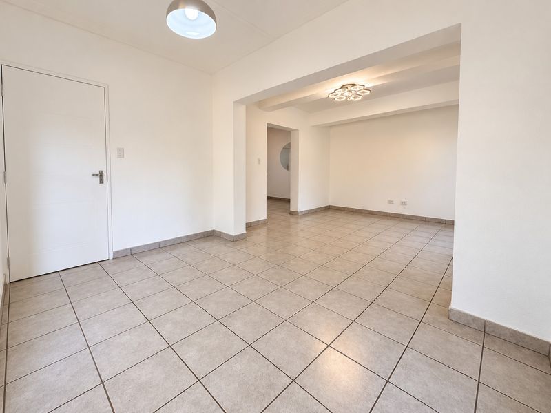 A bright and spacious open-plan living area featuring neutral ceramic floor tiles, clean white walls, and modern ceiling lighting fixtures.