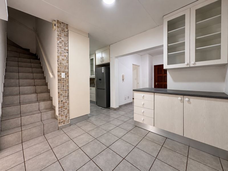 A functional kitchen area featuring tiled flooring, built-in cabinetry with glass-fronted wall units, and a staircase leading to the upper level.
